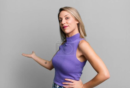 Foto de Blonde adult woman feeling happy and cheerful, smiling and welcoming you, inviting you in with a friendly gesture - Imagen libre de derechos
