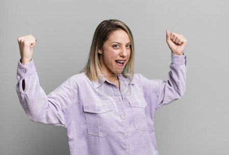 Photo for Blonde adult woman shouting triumphantly, looking like excited, happy and surprised winner, celebrating - Royalty Free Image