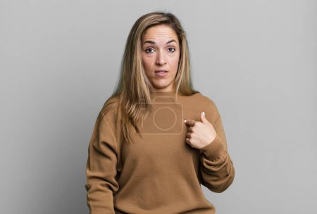 Téléchargez les photos : Blonde adult woman feeling confused, puzzled and insecure, pointing to self wondering and asking who, me? - en image libre de droit