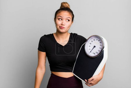 Photo for Hispanic pretty woman shrugging, feeling confused and uncertain. fitness and diet concept - Royalty Free Image