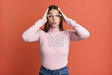 Photo for Pretty young adult woman looking unpleasantly shocked, scared or worried, mouth wide open and covering both ears with hands - Royalty Free Image