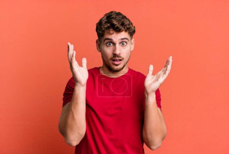 Photo for Young adult caucasian man looking shocked and astonished, with jaw dropped in surprise when realizing something unbelievable - Royalty Free Image