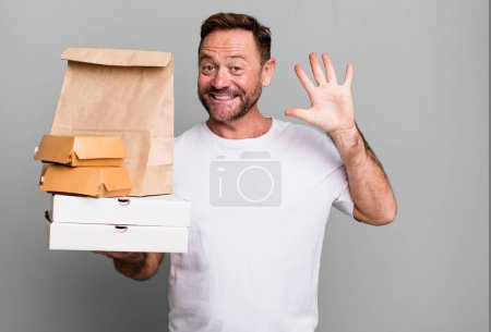 Foto de Hombre de mediana edad sonriendo y buscando amigable, mostrando el número cinco. entrega y comida rápida para llevar concepto - Imagen libre de derechos