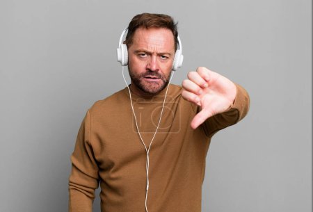 Photo for Middle age man feeling cross,showing thumbs down. listening music with a headphones - Royalty Free Image