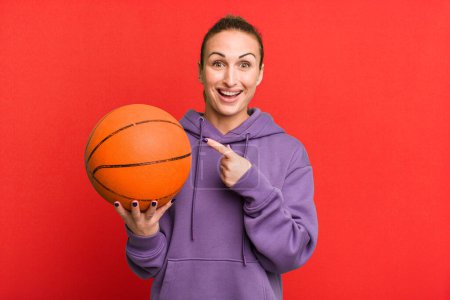 Photo for Young pretty woman looking excited and surprised pointing to the side. basketball concept - Royalty Free Image