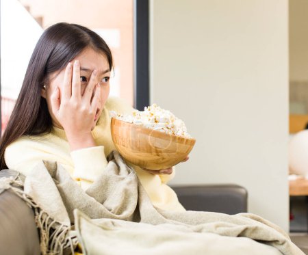 Photo for Asian pretty woman eating popcorns and watching a film at home - Royalty Free Image