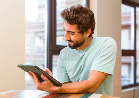 Foto de Young adult bearded man with a touchscreen pad telecommutig concept - Imagen libre de derechos