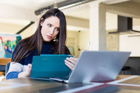Téléchargez les photos : Young adult pretty woman telecommuting with a laptop at home - en image libre de droit