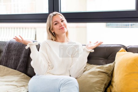 Photo for Young pretty woman feeling puzzled and confused, doubting, weighting or choosing different options sitting on a couch - Royalty Free Image