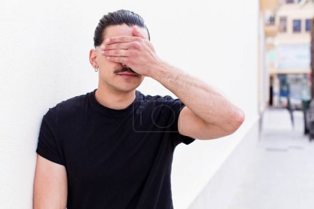 Photo for Young cool man covering eyes with one hand feeling scared or anxious, wondering or blindly waiting for a surprise - Royalty Free Image