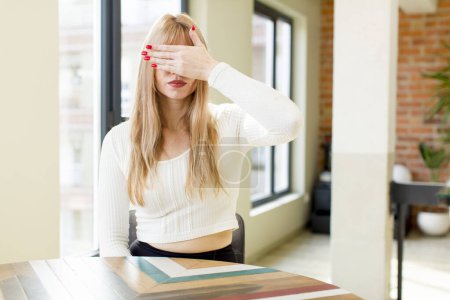 Photo for Young pretty woman covering eyes with one hand feeling scared or anxious, wondering or blindly waiting for a surprise. home interior - Royalty Free Image