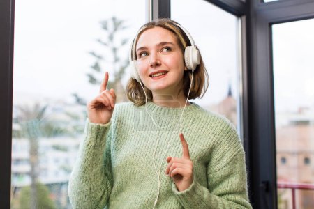 Téléchargez les photos : Jolie jeune femme écoutant de la musique avec des écouteurs. design intérieur de la maison - en image libre de droit