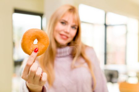 Foto de Una mujer joven y bonita con una rosquilla. concepto de dieta poco saludable en el interior del hogar - Imagen libre de derechos