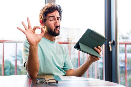 Téléchargez les photos : Young adult bearded man with a touchscreen pad telecommutig concept - en image libre de droit