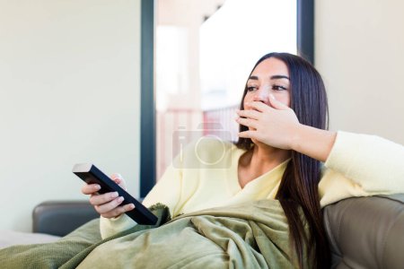 Téléchargez les photos : Jeune jolie femme regarder la télévision et assis sur un canapé à la maison - en image libre de droit