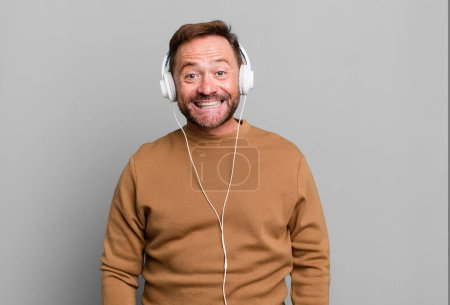 Téléchargez les photos : Homme d'âge moyen l'air heureux et agréablement surpris. écouter de la musique avec un casque - en image libre de droit
