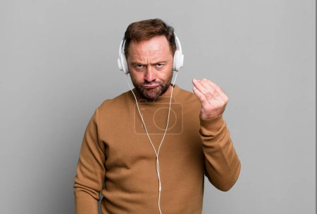 Photo for Middle age man making capice or money gesture, telling you to pay. listening music with a headphones - Royalty Free Image