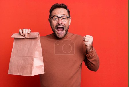 Foto de Hombre de mediana edad sintiéndose sorprendido, riendo y celebrando el éxito. llevar bolsa de papel - Imagen libre de derechos