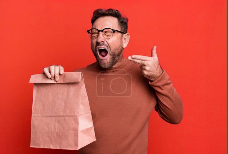 Photo for Middle age man looking unhappy and stressed, suicide gesture making gun sign. take away paper bag - Royalty Free Image