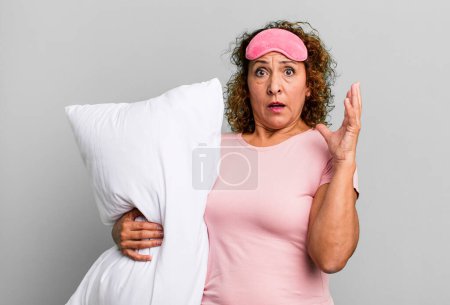 Photo for Pretty middle age woman screaming with hands up in the air wearing pajamas night wear and a pillow - Royalty Free Image