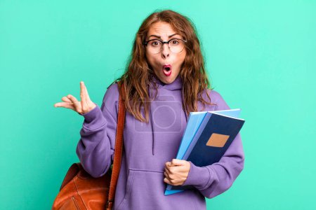 Foto de Hispanic pretty woman looking surprised and shocked, with jaw dropped holding an object. university student concept - Imagen libre de derechos