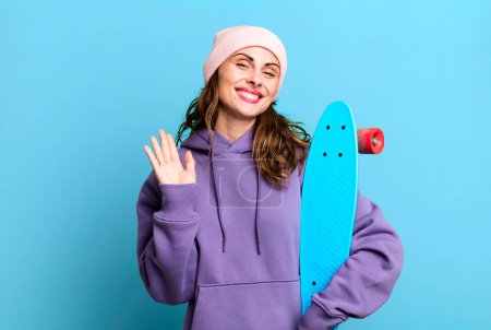 Foto de Bella mujer hispana sonriendo alegremente, saludándote con la mano, dándote la bienvenida y saludándote. concepto de skate boarding - Imagen libre de derechos