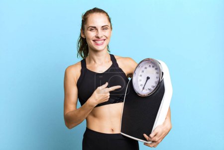 Foto de Hispanic pretty woman looking excited and surprised pointing to the side. fitness, diet and weight scale concept - Imagen libre de derechos