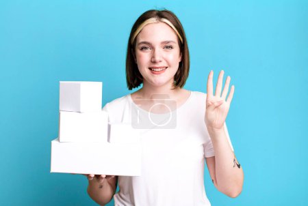 Téléchargez les photos : Jeune jolie femme souriante et sympathique, montrant le numéro quatre. boîtes blanches vides - en image libre de droit