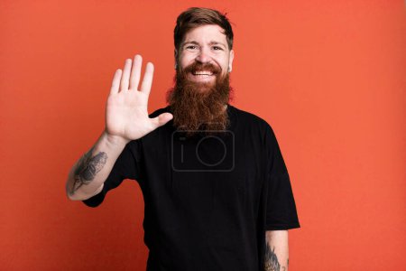 Foto de Barba larga y el hombre de pelo rojo sonriendo felizmente, saludando con la mano, dando la bienvenida y saludando - Imagen libre de derechos