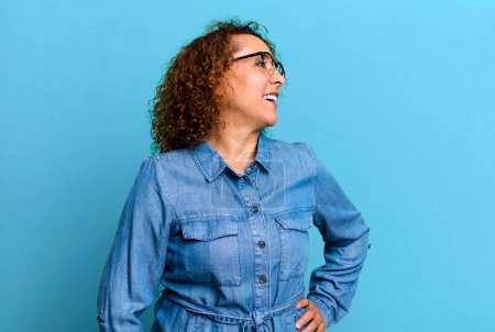Photo for Middle age hispanic woman looking happy, cheerful and confident, smiling proudly and looking to side with both hands on hips - Royalty Free Image