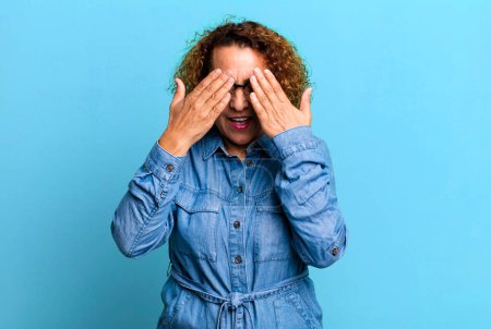 Photo for Middle age hispanic woman smiling and feeling happy, covering eyes with both hands and waiting for unbelievable surprise - Royalty Free Image