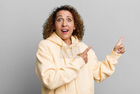 Téléchargez les photos : Femme hispanique d'âge moyen se sentant joyeuse et surprise, souriant avec une expression choquée et pointant vers le côté - en image libre de droit