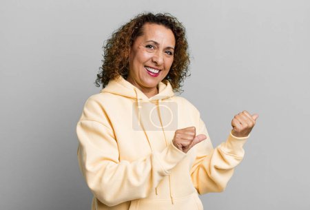 Photo for Middle age hispanic woman smiling cheerfully and casually pointing to copy space on the side, feeling happy and satisfied - Royalty Free Image