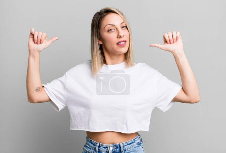 Téléchargez les photos : Blonde femme adulte se sentant fier, arrogant et confiant, regardant satisfait et réussi, pointant vers soi-même - en image libre de droit
