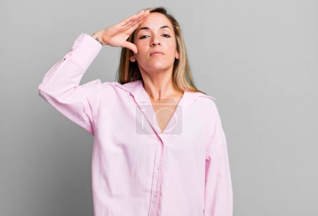 Foto de Blonde adult woman greeting the camera with a military salute in an act of honor and patriotism, showing respect - Imagen libre de derechos
