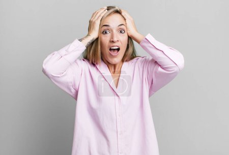 Photo for Blonde adult woman feeling horrified and shocked, raising hands to head and panicking at a mistake - Royalty Free Image