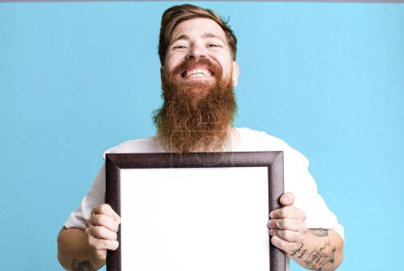 Photo for Young adult red hair bearded cool man holding an empty picture frame - Royalty Free Image