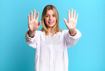 Foto de Rubia bonita mujer sonriendo y buscando amigable, mostrando el número diez o décimo con la mano hacia adelante, cuenta atrás - Imagen libre de derechos