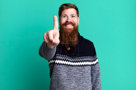 Téléchargez les photos : Barbe longue et cheveux roux homme souriant fièrement et en toute confiance faisant numéro un - en image libre de droit