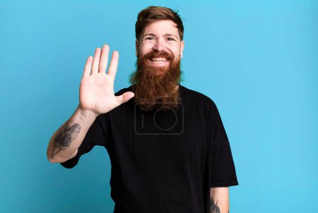 Foto de Barba larga y el hombre de pelo rojo sonriendo felizmente, saludando con la mano, dando la bienvenida y saludando - Imagen libre de derechos