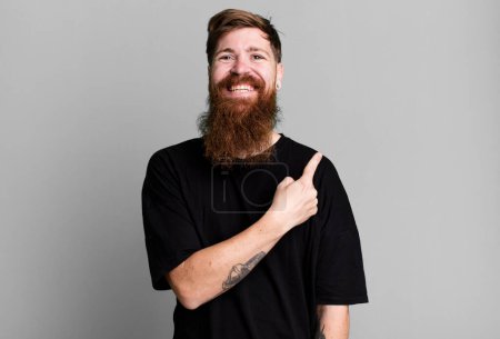 Photo for Long beard and red hair man smiling cheerfully, feeling happy and pointing to the side - Royalty Free Image