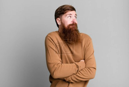 Foto de Barba larga y cabello rojo hombre encogiéndose de hombros, sintiéndose confundido e incierto - Imagen libre de derechos