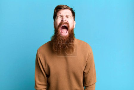 Foto de Barba larga y pelo rojo hombre gritando agresivamente, mirando muy enojado - Imagen libre de derechos