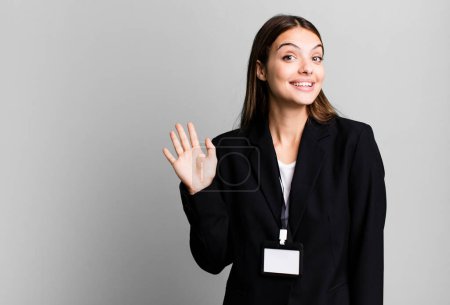 Téléchargez les photos : Young pretty woman smiling happily, waving hand, welcoming and greeting you. businesswoman concept - en image libre de droit