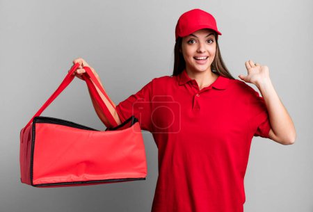 Foto de Young pretty woman smiling happily, waving hand, welcoming and greeting you. pizza delivery concept - Imagen libre de derechos