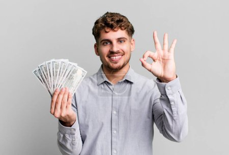Foto de Joven adulto caucásico hombre sintiéndose feliz, mostrando aprobación con buen gesto. dólar concepto de billetes de banco - Imagen libre de derechos