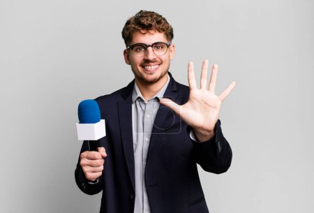 Téléchargez les photos : Jeune homme caucasien adulte souriant et regardant amical, montrant numéro cinq. journaliste ou présentateur avec un microphone - en image libre de droit