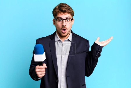Téléchargez les photos : Young adult caucasian man looking surprised and shocked, with jaw dropped holding an object. journalist or presenter with a microphone - en image libre de droit