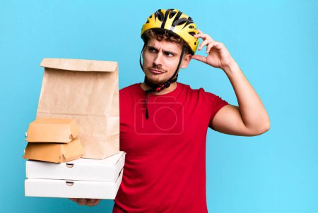 Téléchargez les photos : Young adult caucasian man smiling happily and daydreaming or doubting.  take away fast food deliveryman concept - en image libre de droit
