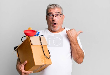 Foto de Hombre mayor de mediana edad mirando asombrado en la incredulidad. ama de llaves reparador con un concepto de caja de herramientas - Imagen libre de derechos